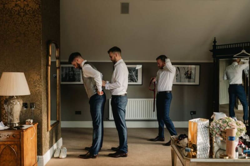 The groomsmen help the groom get dressed.