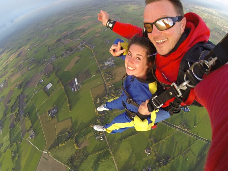 Man and woman in overalls skydiving over countryside