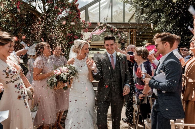 Newlywed couple exit the ceremony area whilst guests throw flower petals.