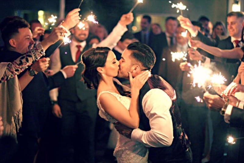 A couple is kissing while guests are holding lights around them.