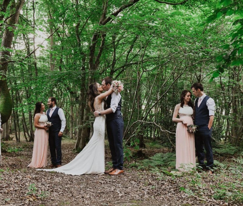 The bride and groom kiss while the bridesmaids and groomsmen stand close to each other.