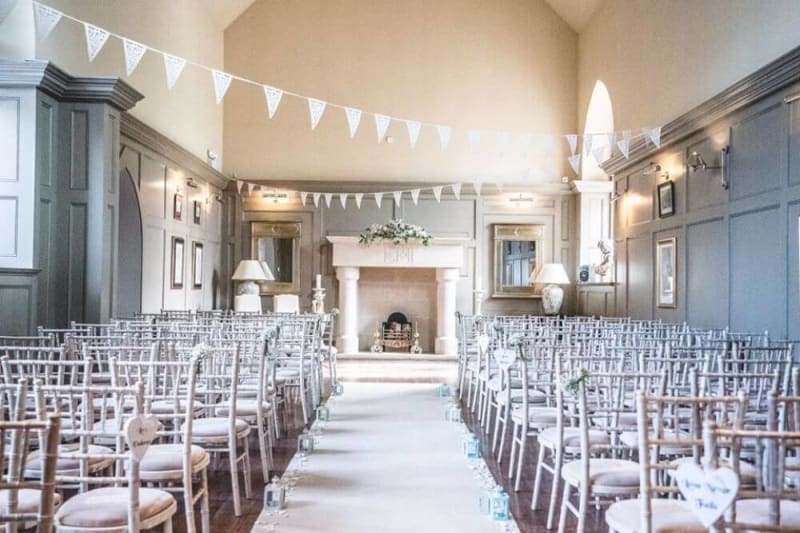 A white hall with a fireplace in the back. Several chais are lined up for a wedding.