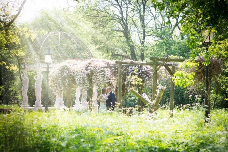 Bride and groom kissing in the middle of a garden with sunshine coming down on them.