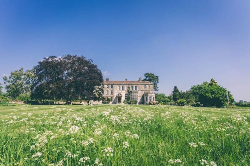 Manor house venue photo taken from far away from a field of flowers on a sunny day.