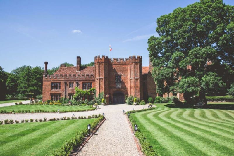 A brickhouse tudor style mansion is shown across well kept lawns.