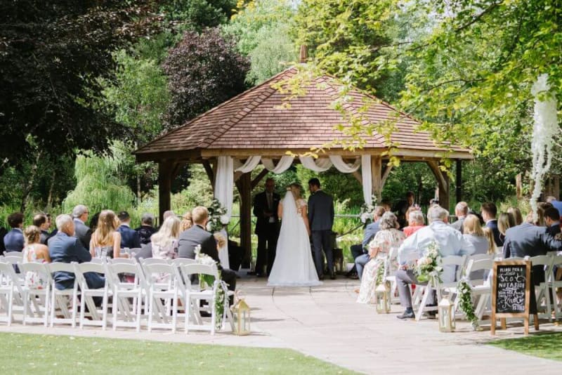 Wedding ceremony under a gazebo outside on a sunny day.