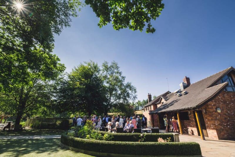 Wedding guests in the garden outside a wedding venue on a sunny day.