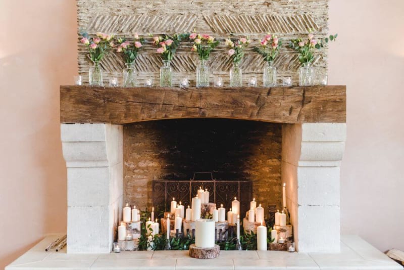 A variety of candles stands inside a white fireplace.