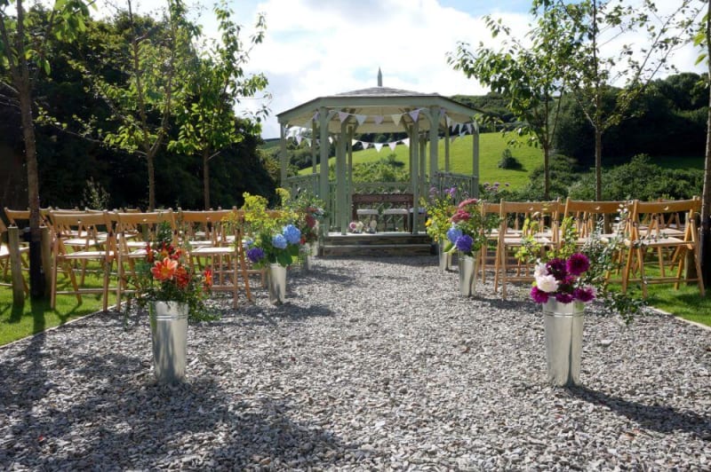 A green garden gazebo surrounded by wooden chairs.