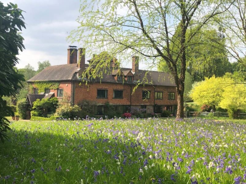 A brick house stands in a meadow filled with flowers and greenery.