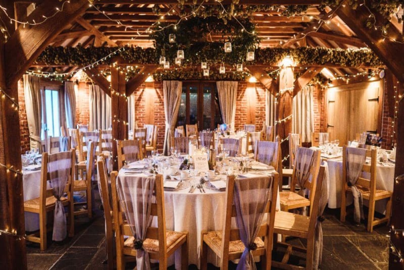 Inside shot of the reception room filled with wooden tables and chairs with lights adorning the beams.