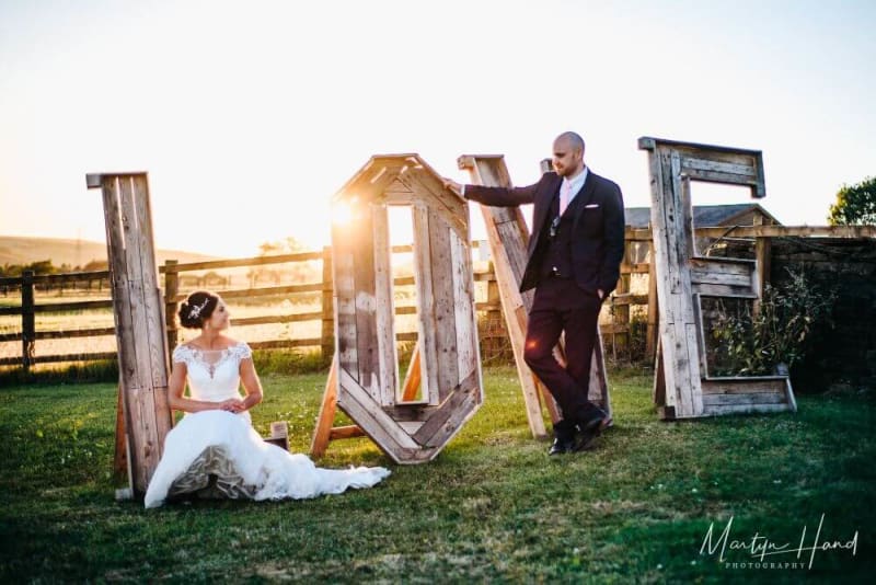 A bride and groom in front of a large 'LOVE' sing made out of wood.