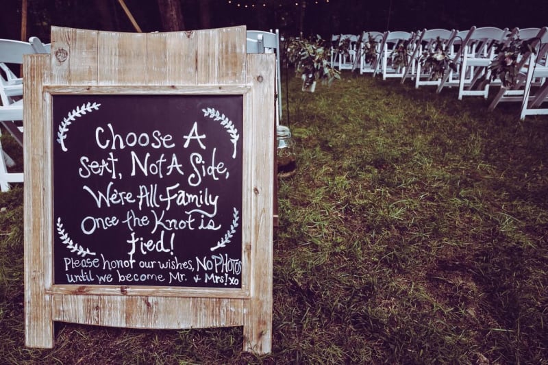 Wedding chalkboard sign next to wedding aisle at outdoor wedding