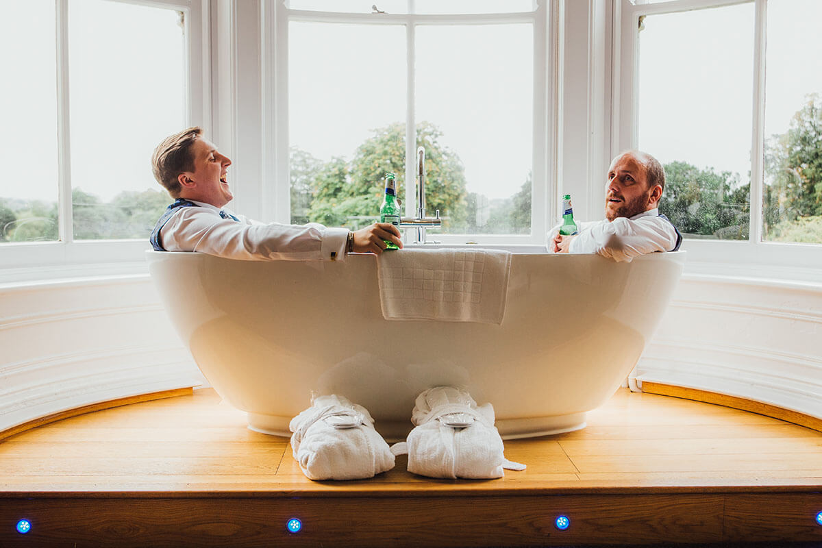 two groomsmen lauging in an empty bathtub and having a beer, best wedding photos of 2018