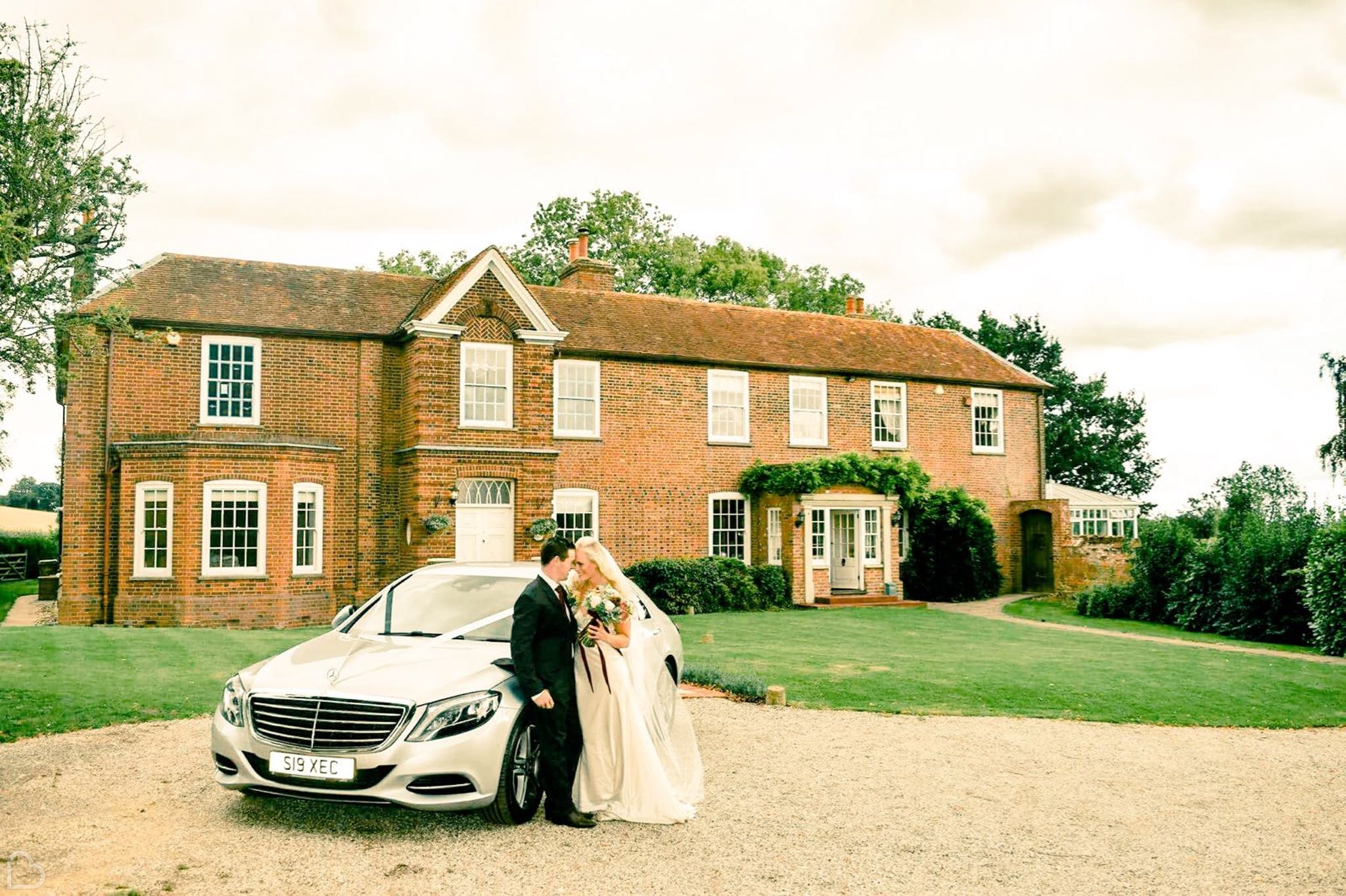 Newlyweds sit on wedding car in front of Downham Hall Wedding Venue in Essex