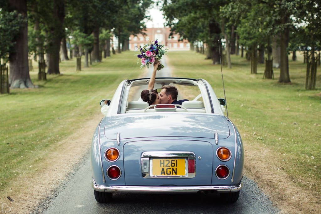 Newlyweds drive down the road at Helmingham Hall Gardens. 