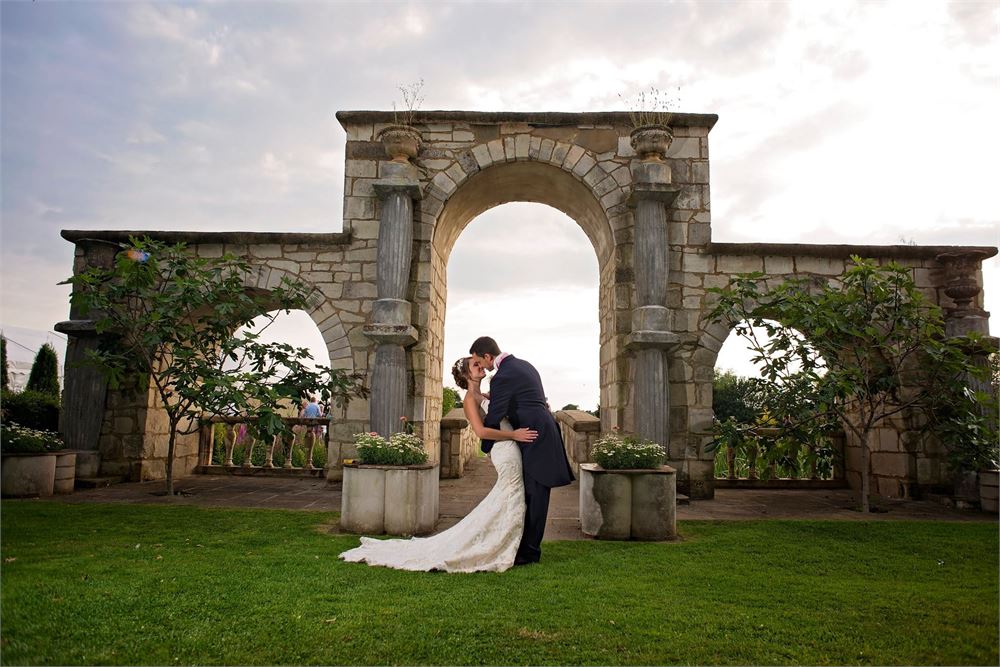 Newlyweds kiss in front of arched balcony, at flaxbourne gardens.