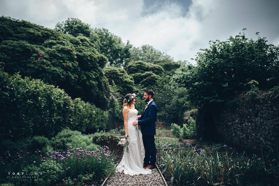 Newlyweds walk through the pathway surrounded by greenery, in Knightor Winery.