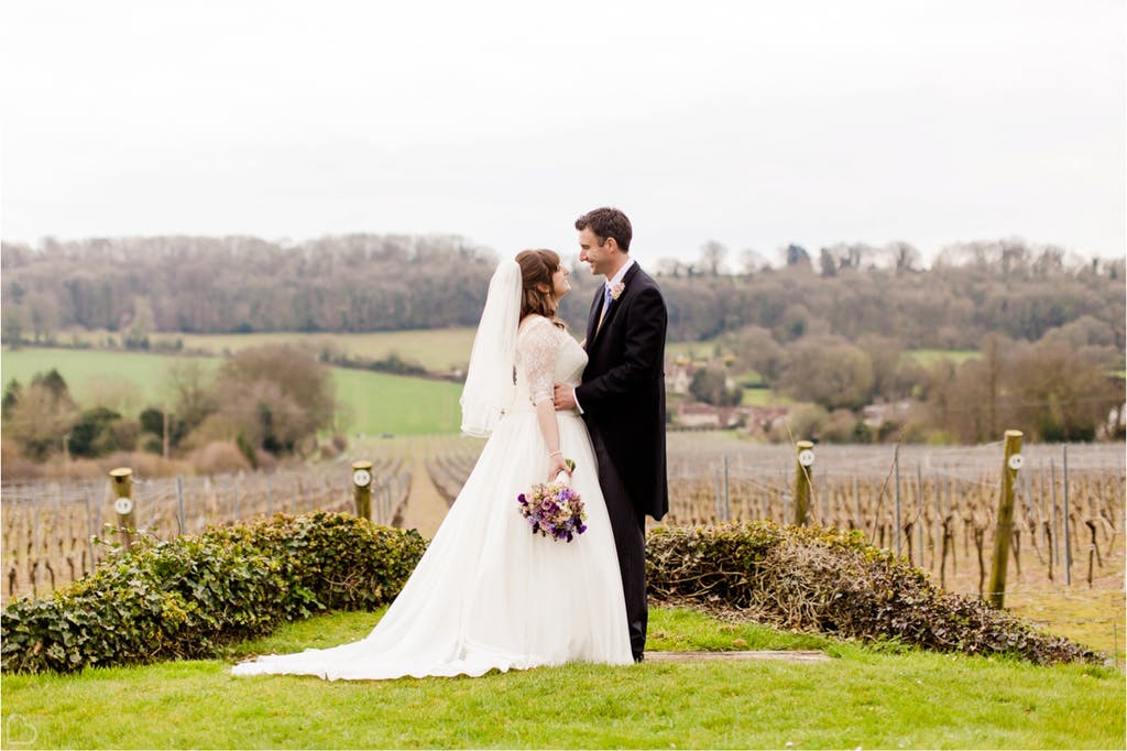 Couple poses happily in from of the vineyard on a foggy day.