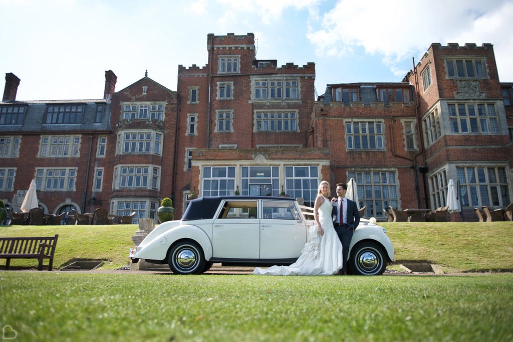 newlyweds pose with their classic car in front of seldsdon park hotel & golf club