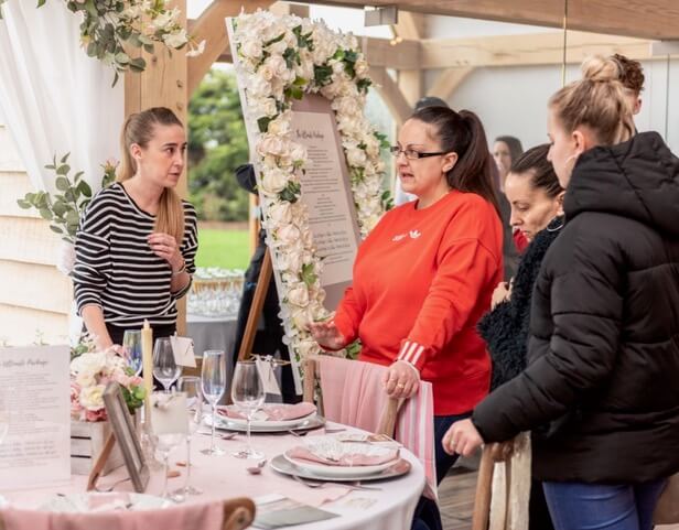 Four women standing and talking around a table set up at a wedding showcase. 