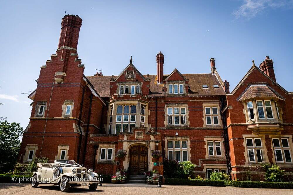 Photograph of a red brick country house with a classic car in front of it. 