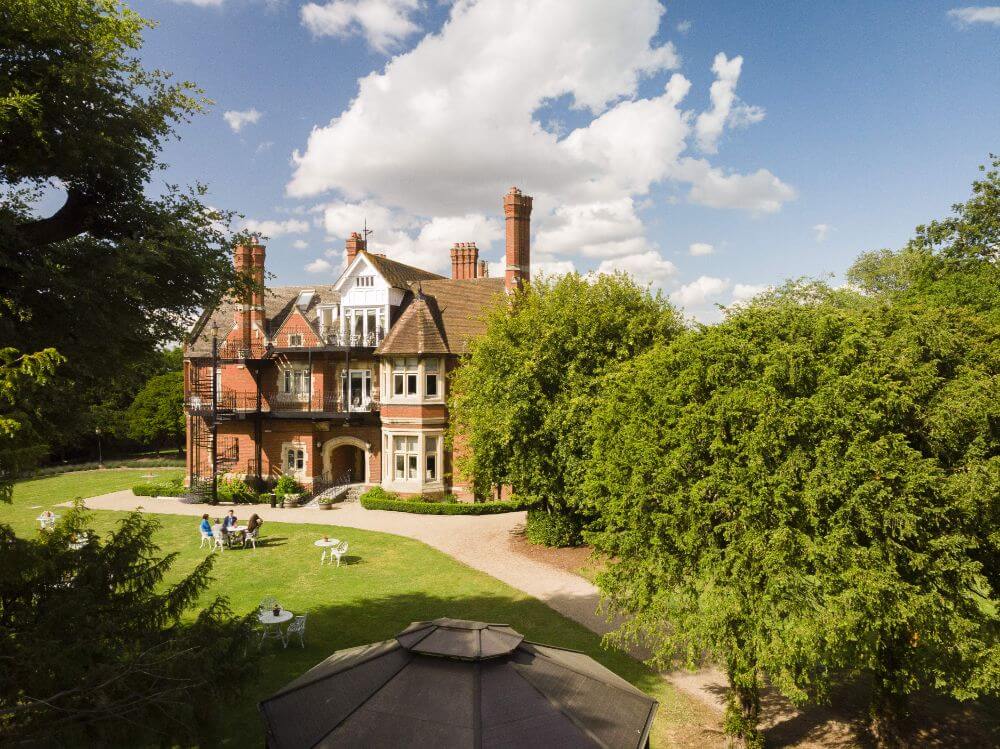 A far away shot through the trees of a red brick country house on a sunny day.