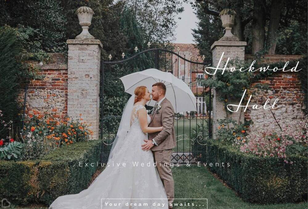 The bride and groom stand outside holding an umbrella and embracing.