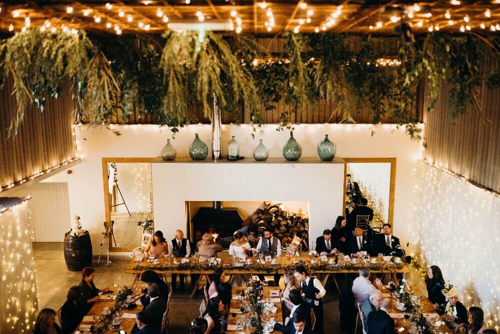 the reception room with four long wooden tables where people are seated. The room is covered in tiny lights.