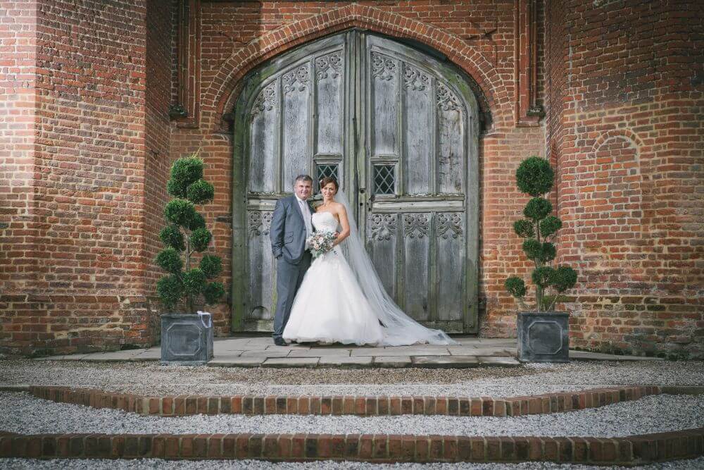 Bride and Groom stand in front of a big door filled with intricate details.