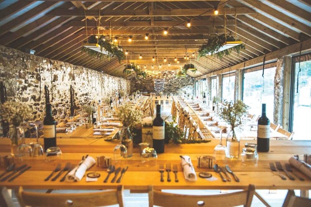 A long stone room with an oak beam ceiling with a table in the centre.