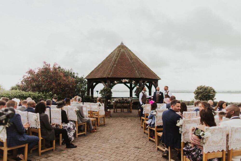 The Brown Gazebo in the garden surrounded by chairs filled with people waiting.