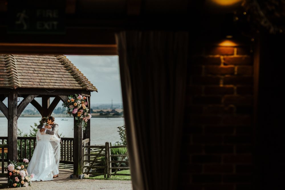 The bride and groom embracing outside under the wooden gazebo.