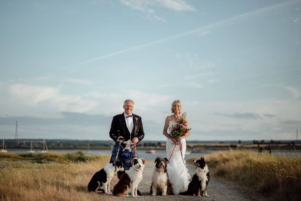 Bride and Groom stand with 4 dogs smiling.