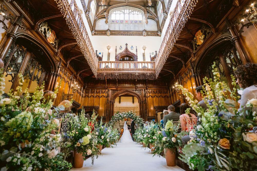 Bride and groom standing under a floral archway with guests on either side of the aisle. 