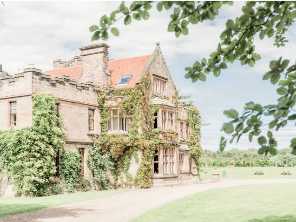 A Big Stone house with a rustic style covered in plants from the roof to the ground.