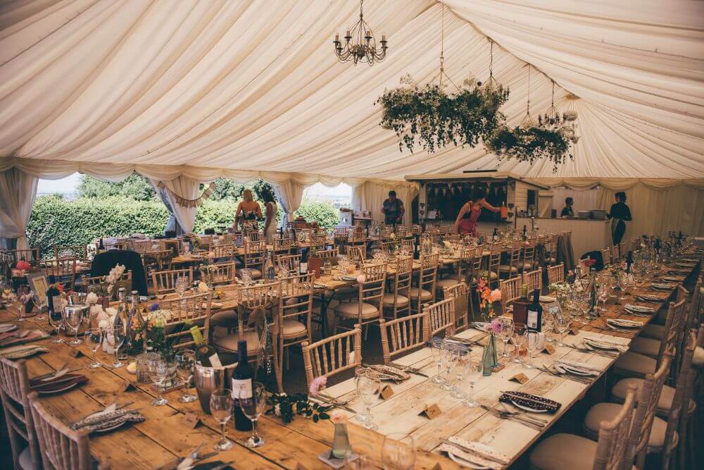 Inside of a white tent. Four long wooden tables are set for the dinner.