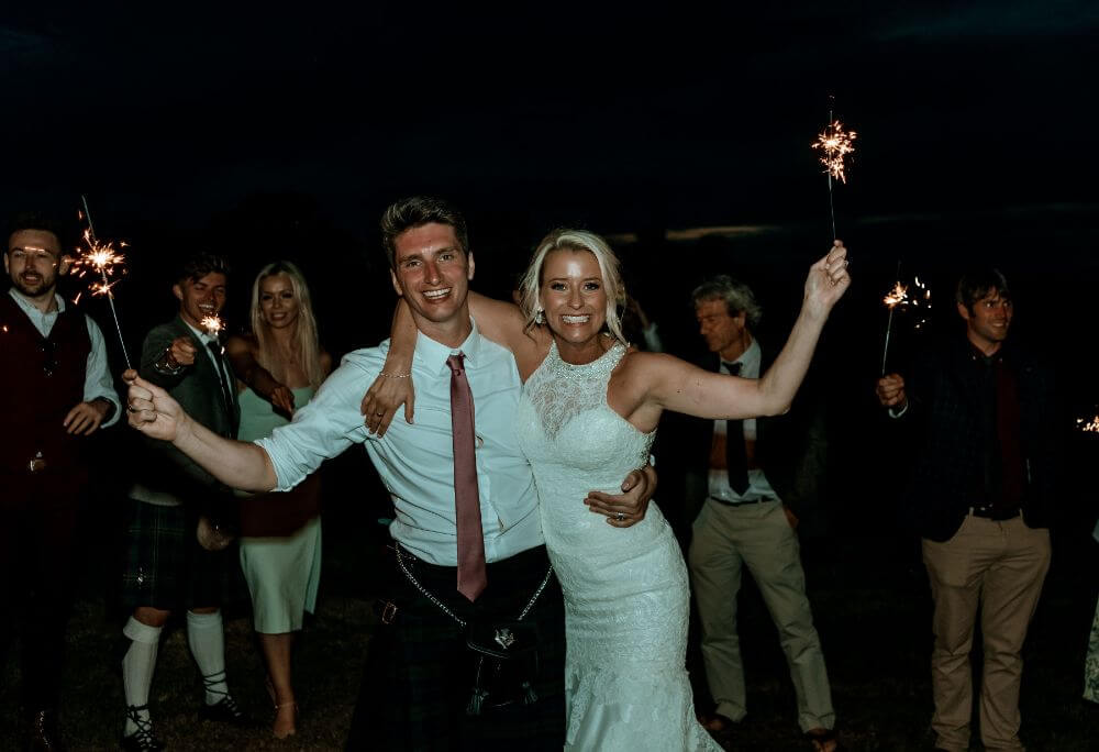 A newlywed couple hold sparkles while smiling.