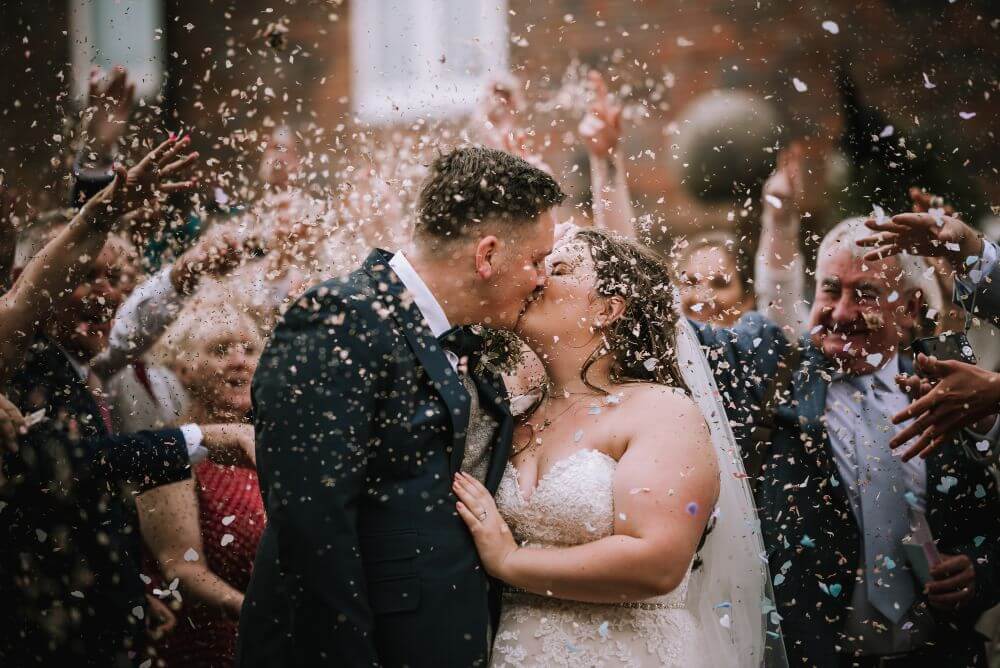 The bride and groom kiss as petals are thrown at them.
