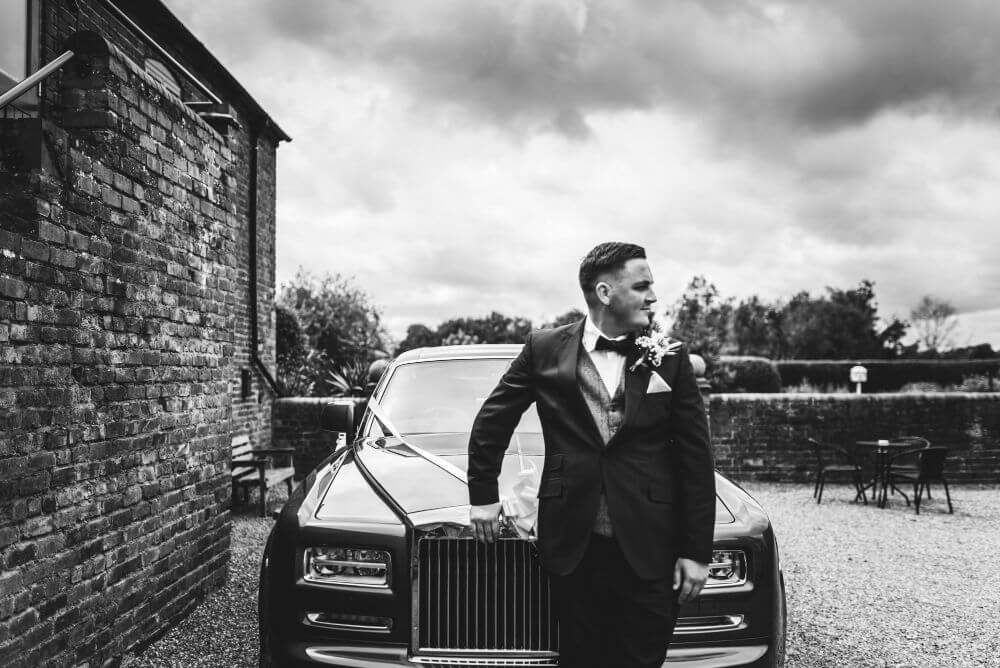 The groom leaning against a car.