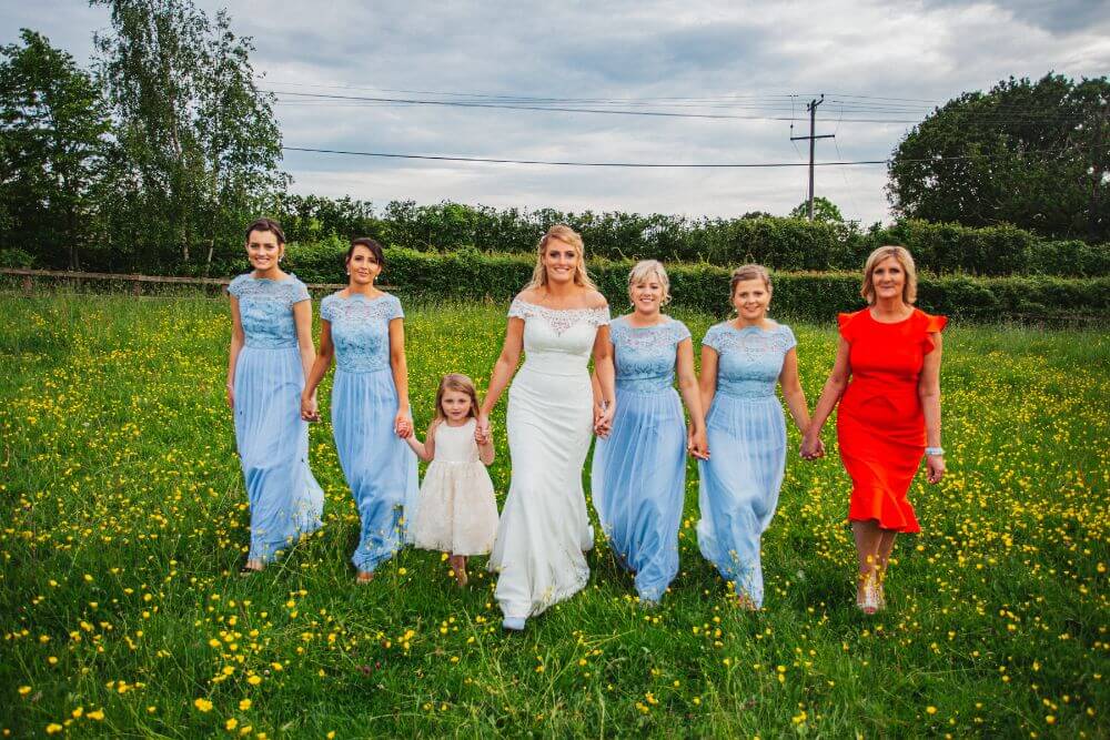 The bride holding hands with several women in blue and red and a little girl in white.