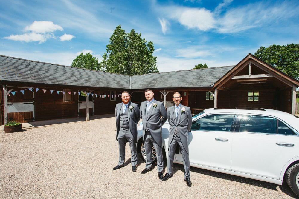 The groom and groomsmen stand next to a white car.