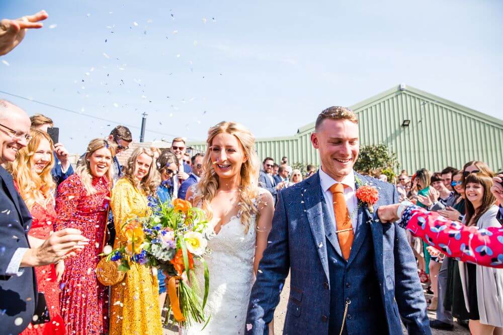 The bride and groom outside walking as people throw petals.