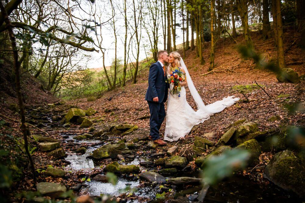 The couple kiss beside a stream in the woods.