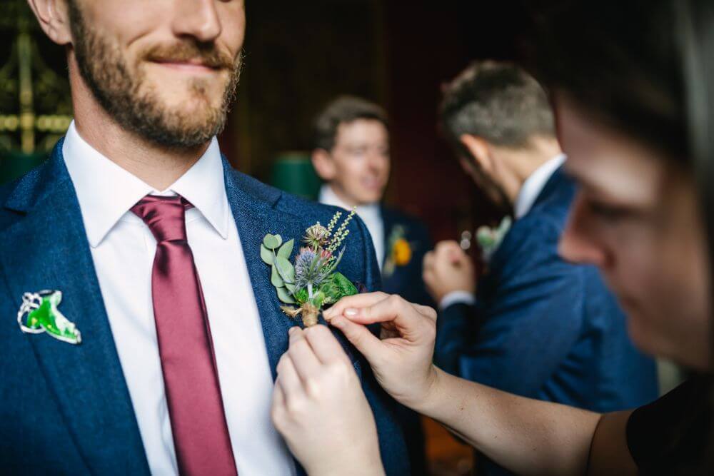 A lady fixes the flowers in one of the groomsmen jacket.