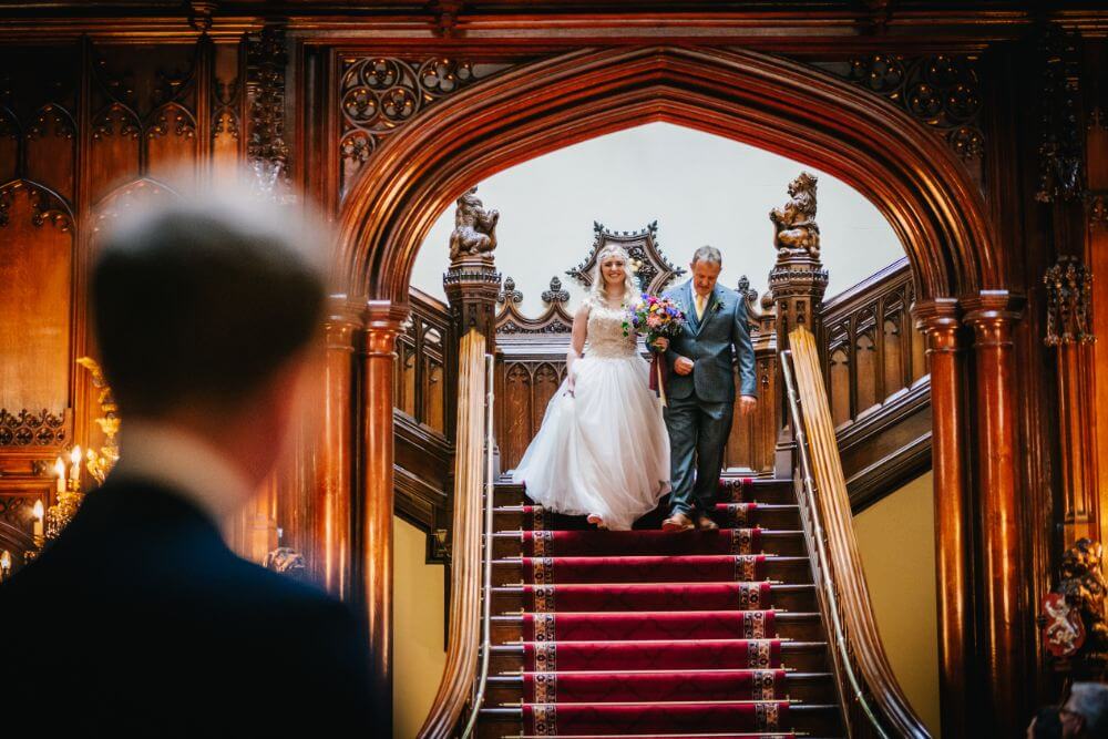 The bride and her father walk down a red staircase.