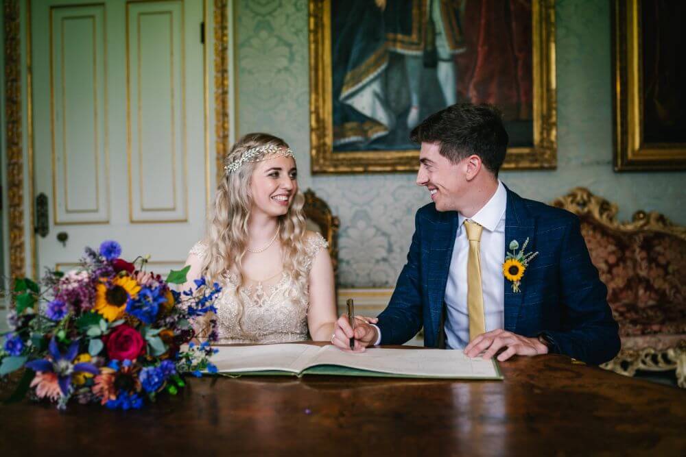 The bride and groom smile at each other as they sign the papers.