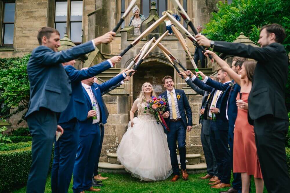 The bride and groom walk underneath cricket bats held by their guests.