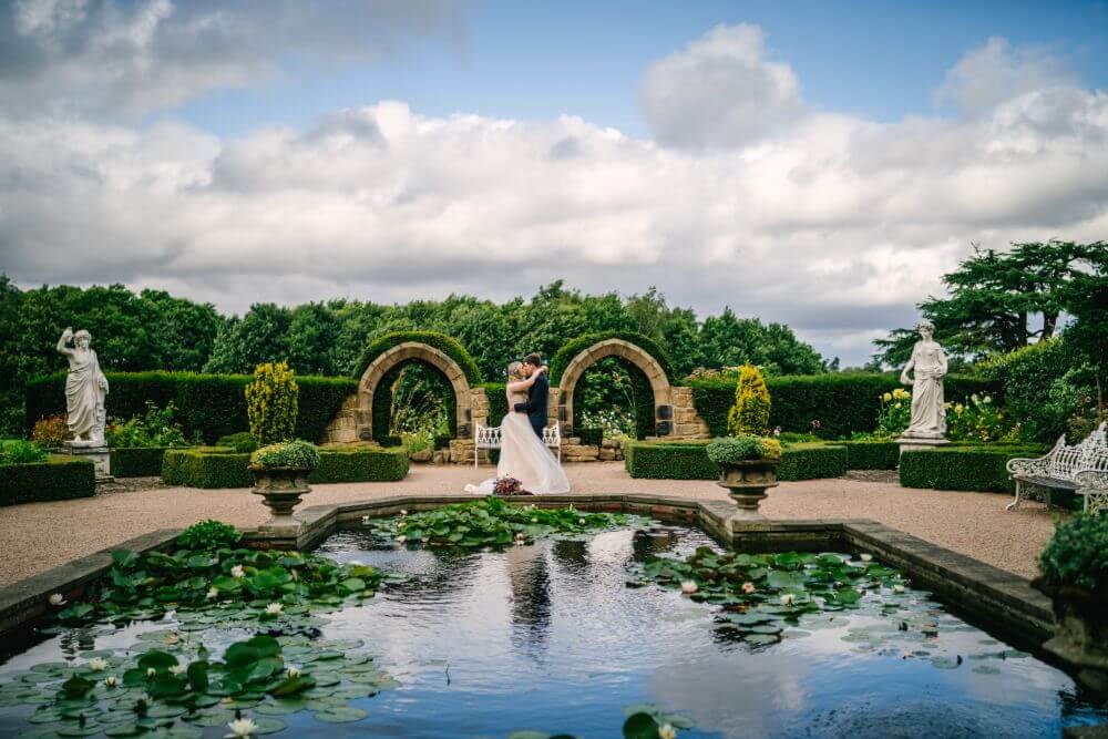 The bride and groom kiss beside a pond.