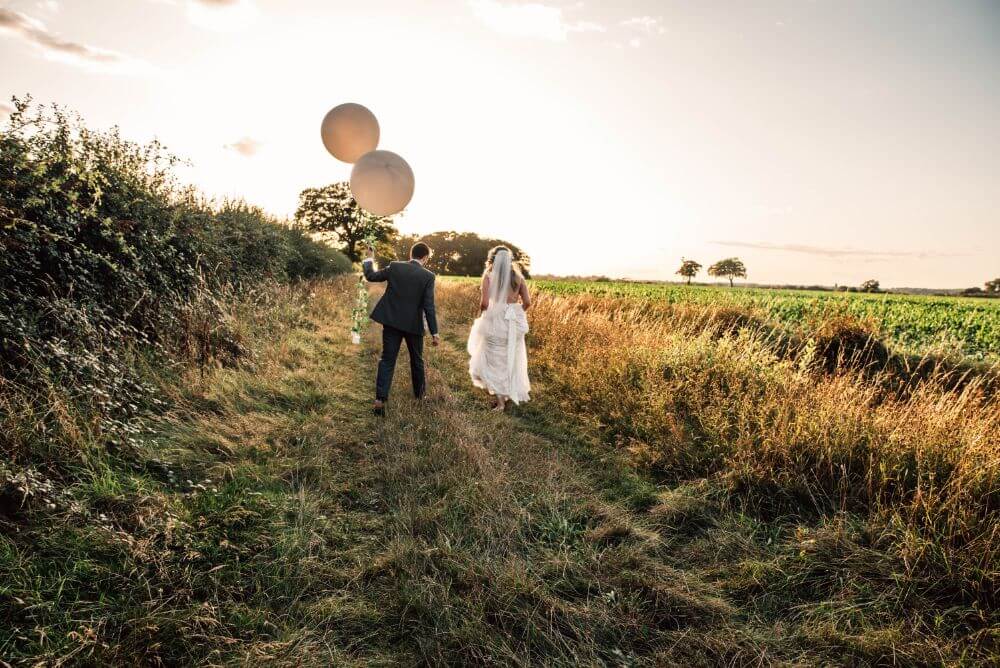 The bride and groom running outside as the groom holds two big white ballons.